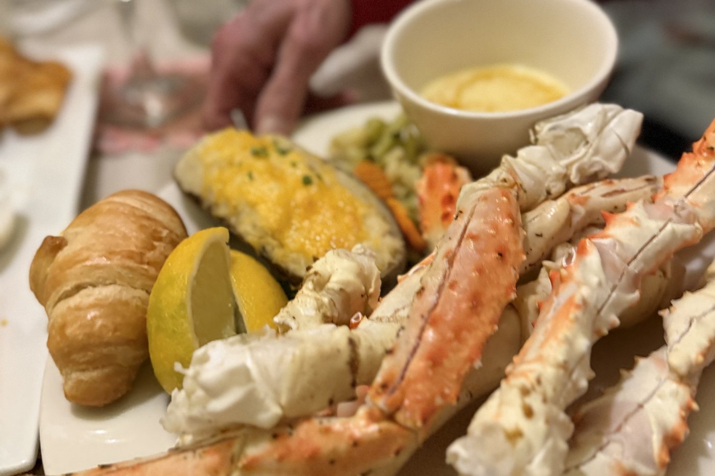 A plate of crab legs with drawn butter, a cheesy twice-baked potato, sauteed vegetables and a warm croissant on a table at The Emporium
