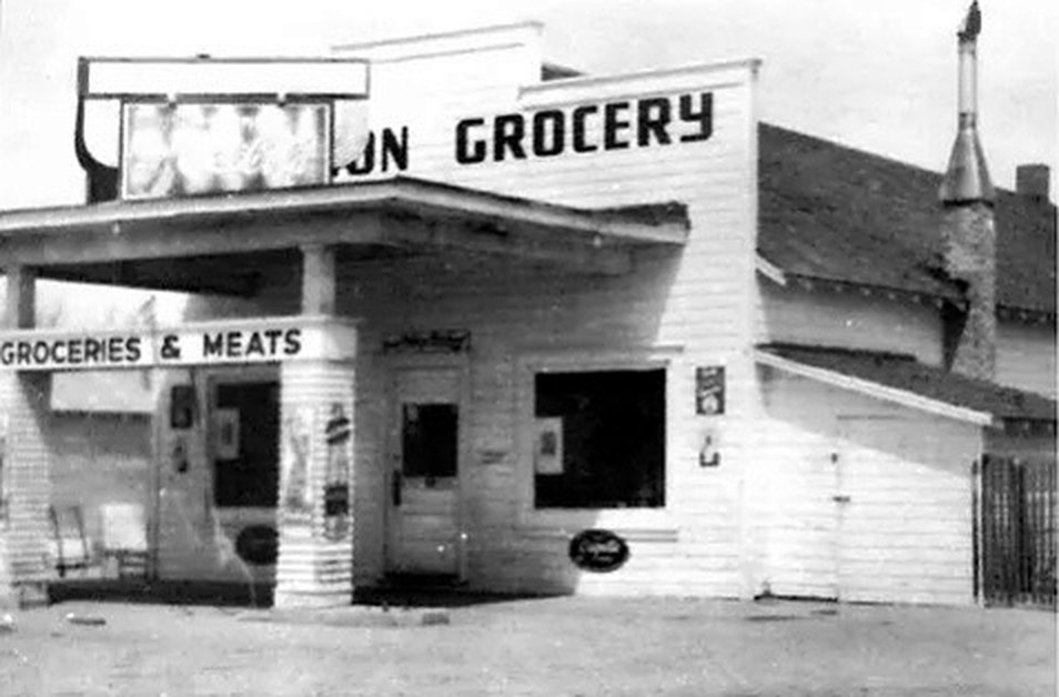 Archive photograph of Swanson Grocery: a false-front wooden store with a canopy over the entrance and signs reading GROCERY and GROCERIES & MEATS